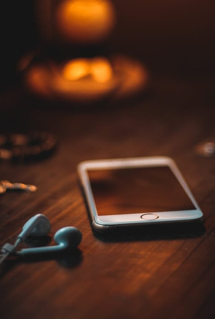 Contáctanos. Mobile phone with earphones on a wooden table in warm ambient light, creating a cozy atmosphere.
